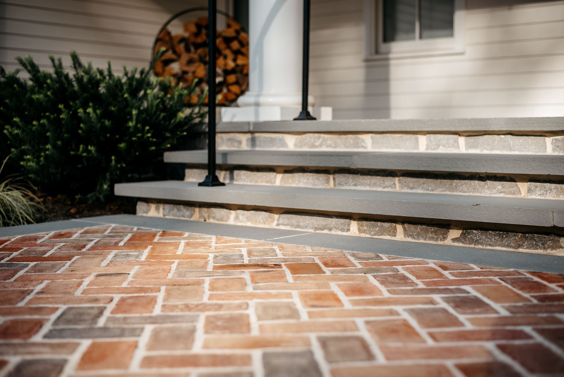 Brick front porch with white steps, black railing, and green shrubs beside a house