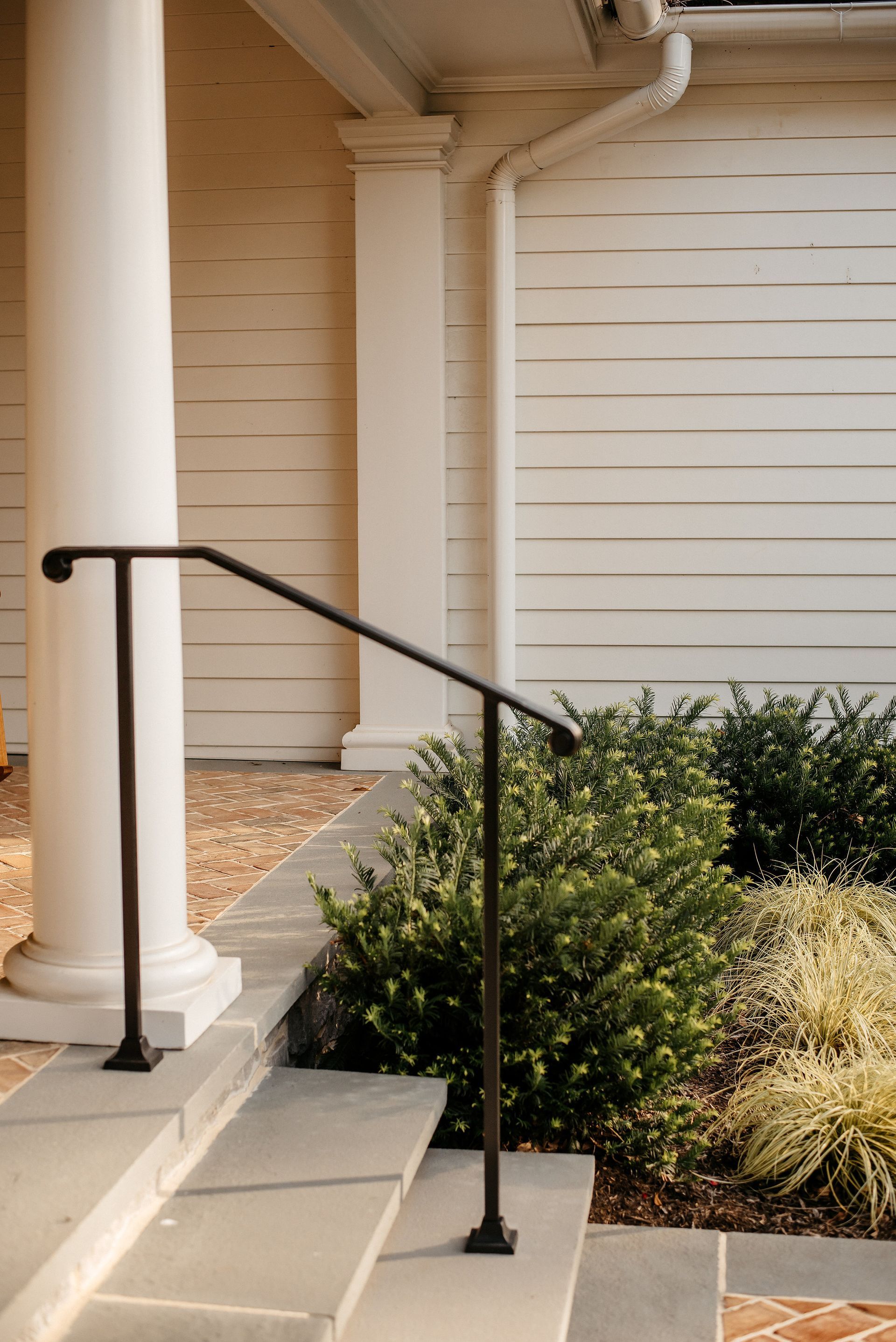 Exterior steps with black handrail beside a tan building and shrubs