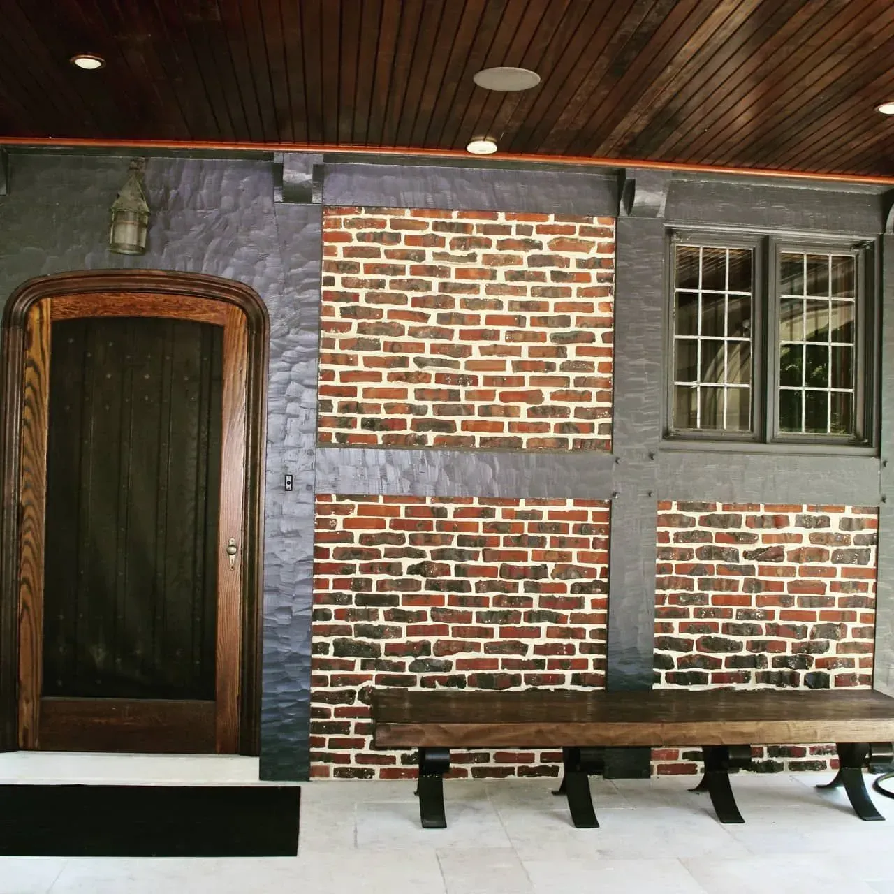 Brick interior wall with arched wooden door and a long bench under windows