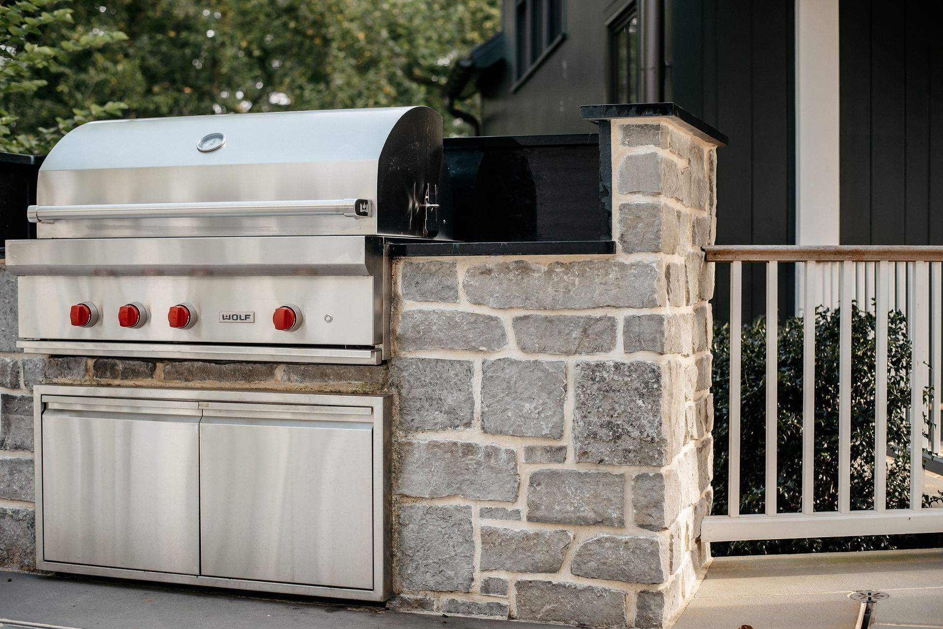 Stainless steel outdoor grill beside a stone wall and white gate