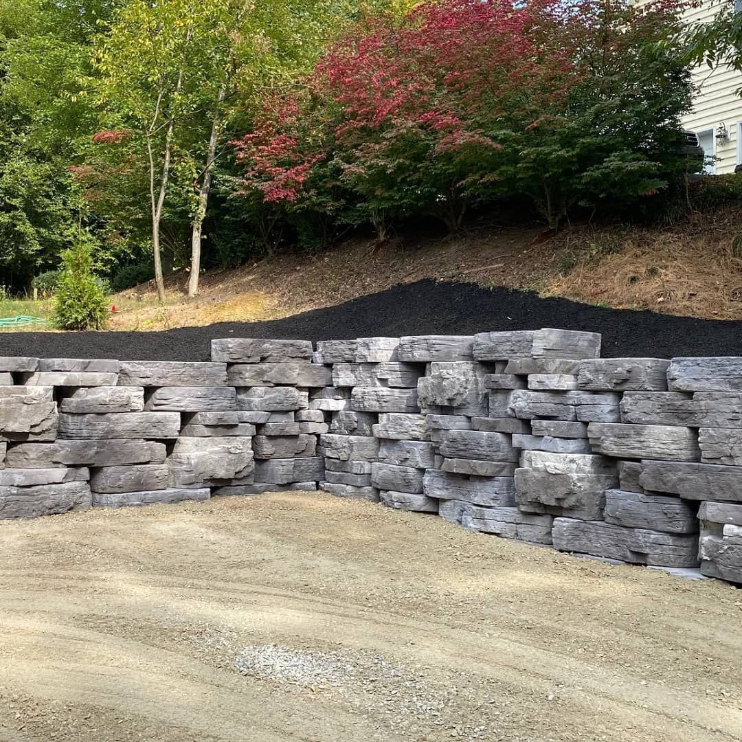 Stone retaining wall beside a gravel drive with mulched slope and trees in the background