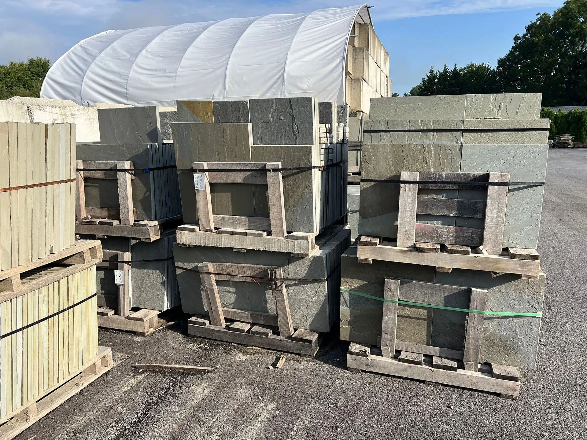 Stacks of concrete blocks on pallets in an outdoor industrial yard, with a white covered structure in back.