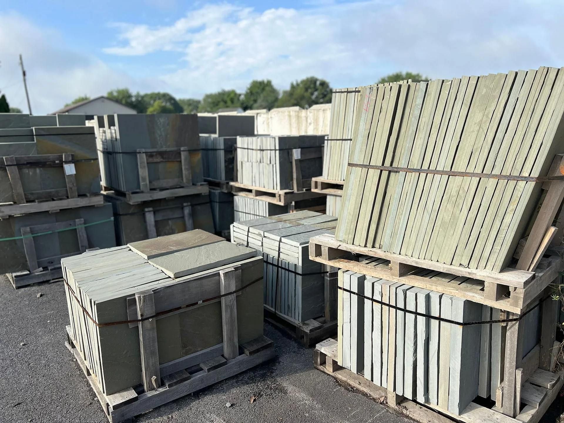 Stacks of gray concrete blocks strapped on pallets in an outdoor storage yard under a blue sky