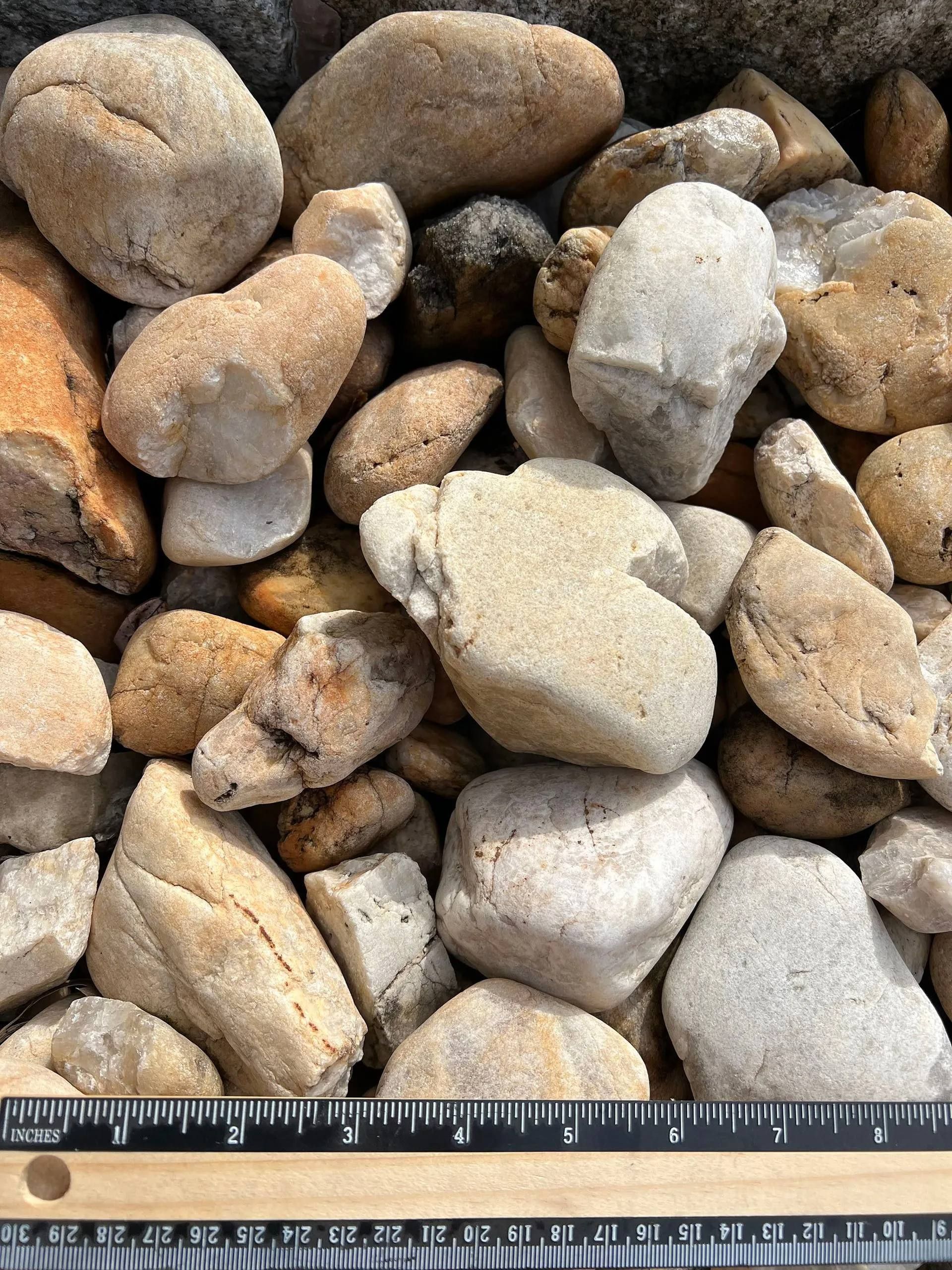 Close-up of assorted rounded rocks and pebbles in tan, gray, and white, with a ruler along the bottom edge.