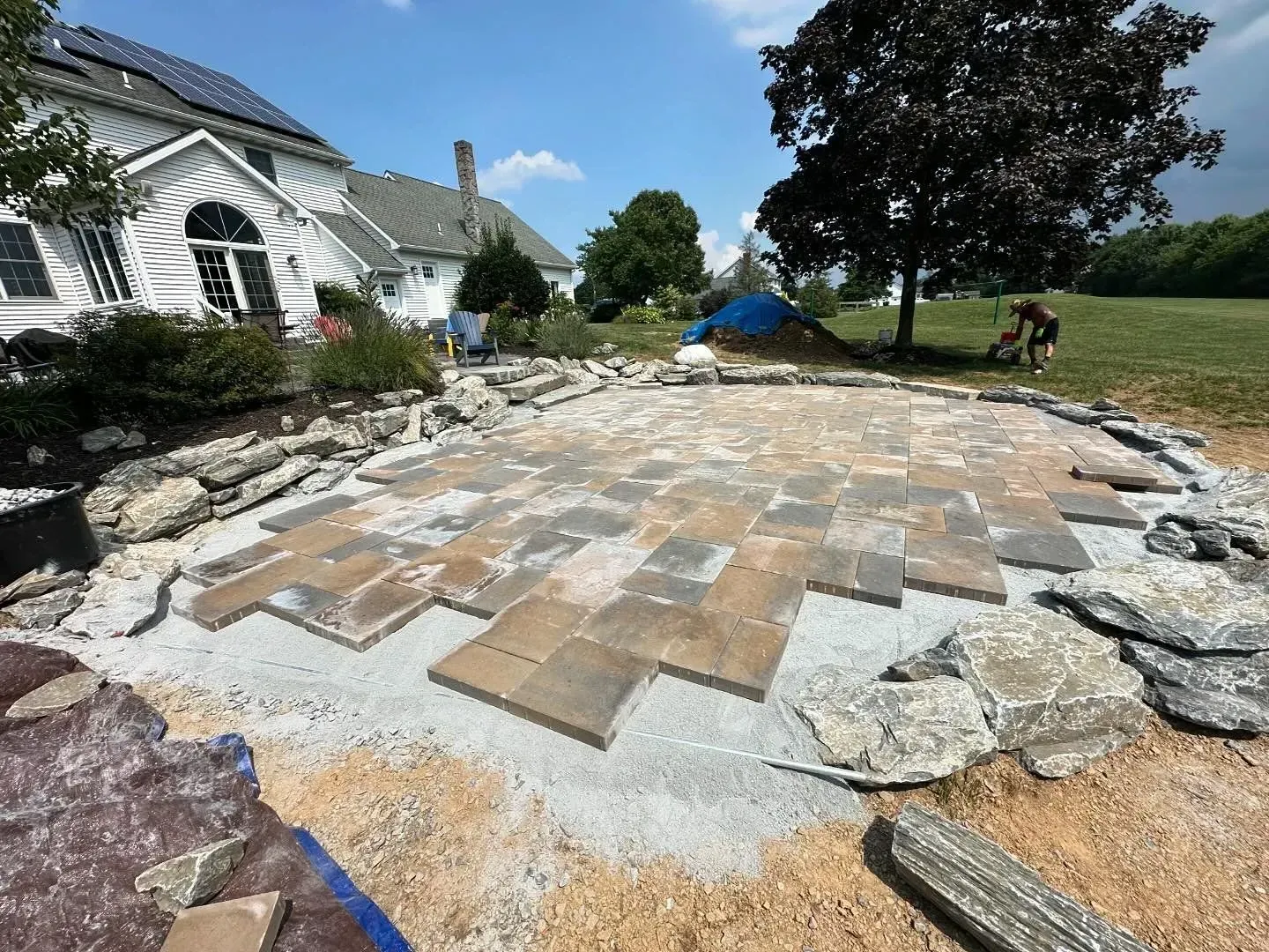 Patio under construction beside a house, with stone pavers laid on gravel and debris around the edges