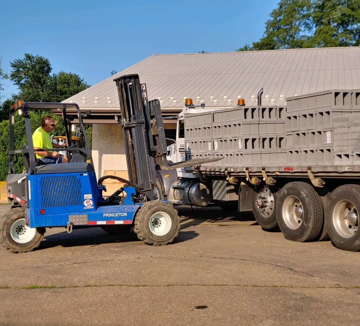 Blue forklift loading gray concrete blocks onto a flatbed trailer outside a building