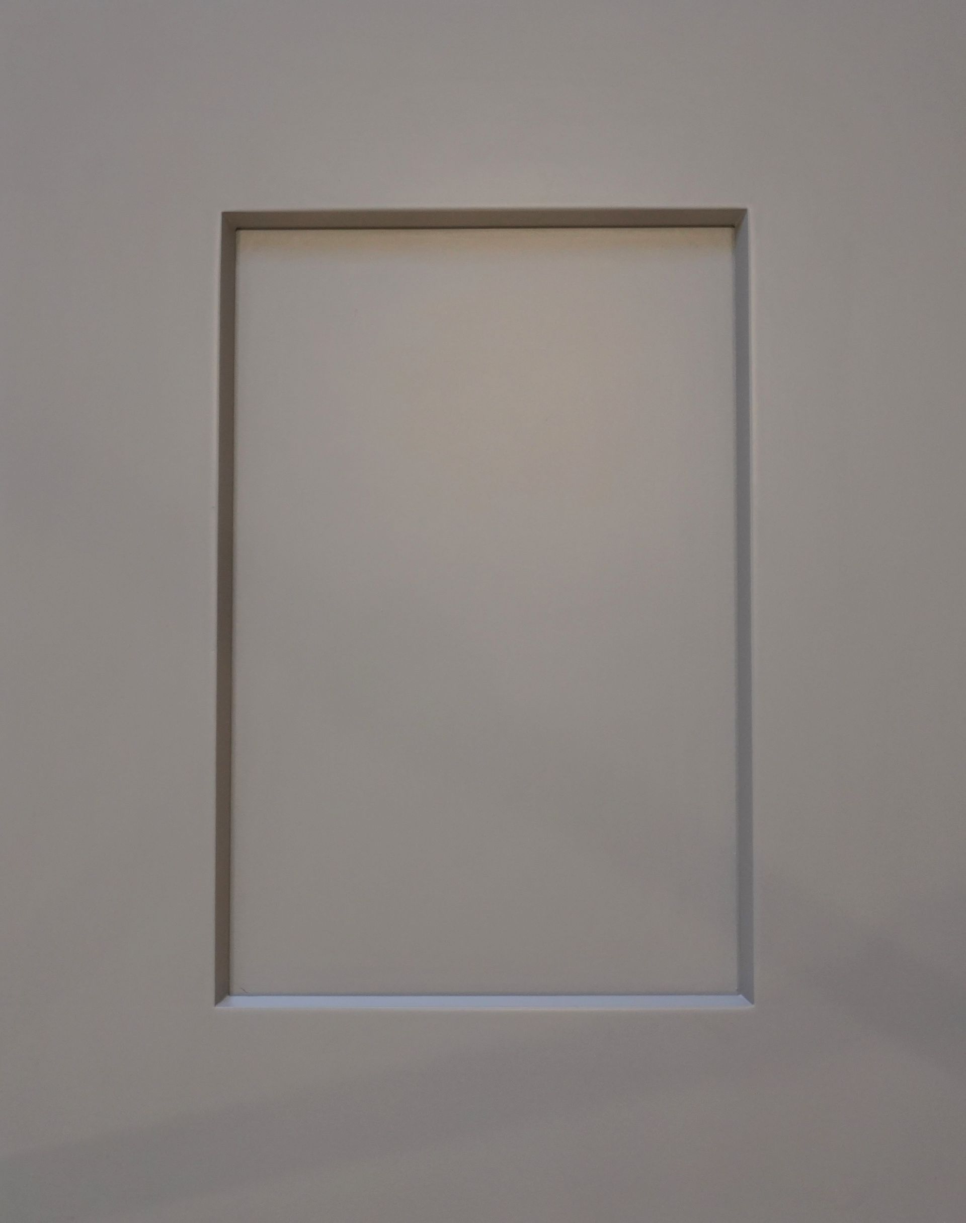 Empty rectangular wall recess with a light-colored frame on a plain gray wall.