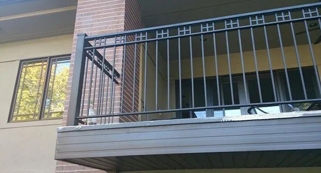 Apartment balcony with gray railing beside a brick building and windows