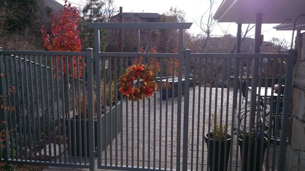 Iron gate entrance with a red-orange wreath, leading to a paved courtyard and potted plants under a sunny sky