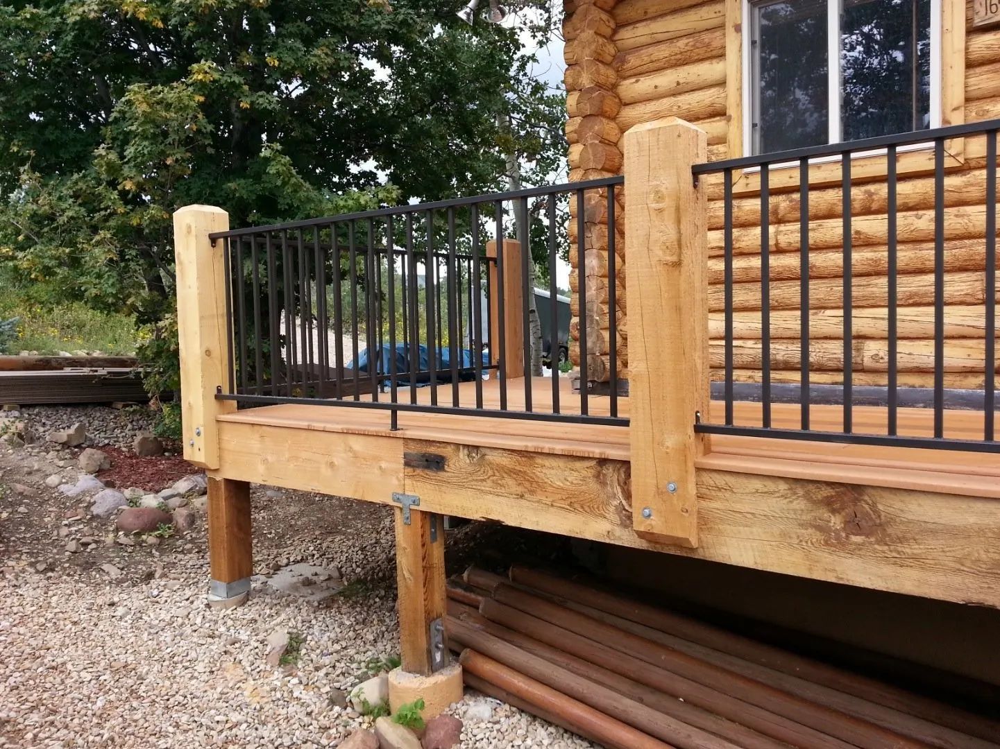 Wooden cabin deck with black metal railing and stairs, seen from the side outdoors