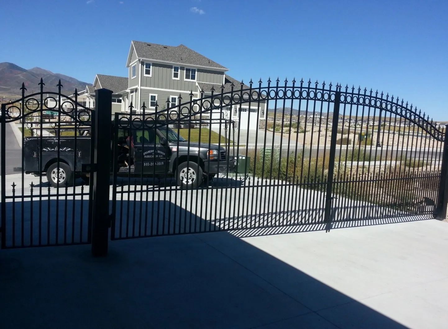 Black wrought-iron gate in front of a house with a pickup truck and mountains in the background