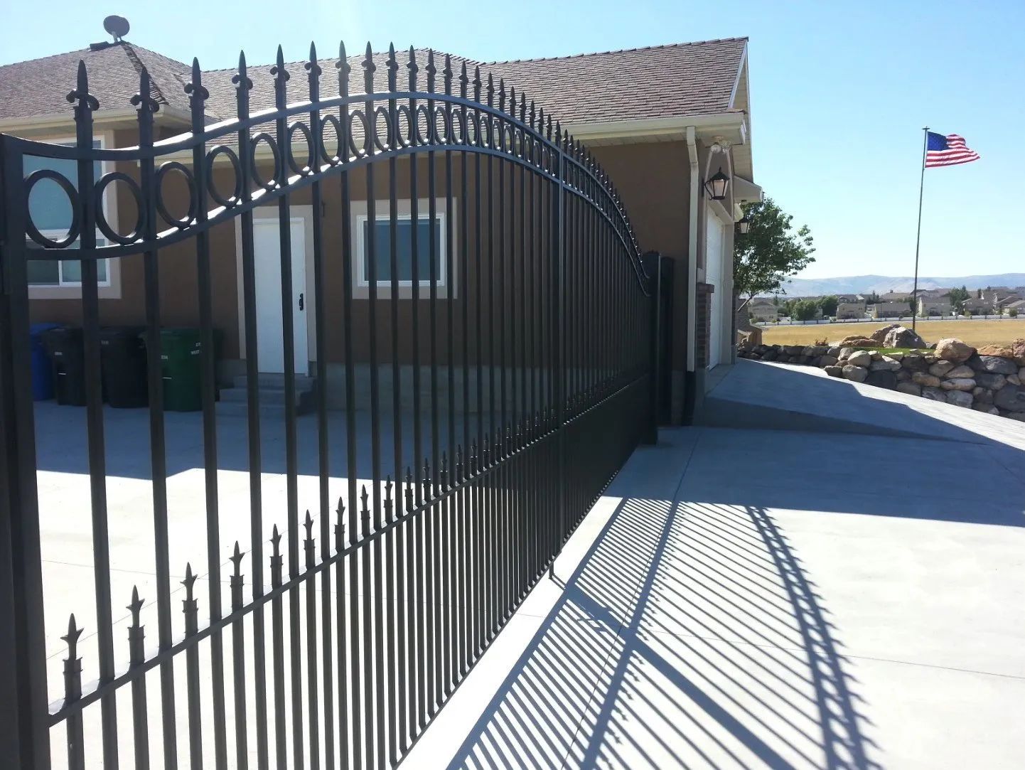Black iron gate beside a house driveway, with an American flag and desert landscape in the background