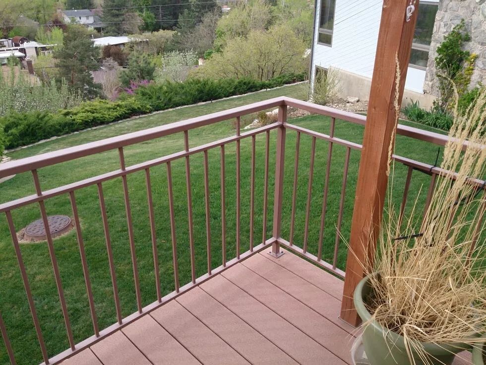 Wooden deck with brown railing overlooking a green lawn and garden.