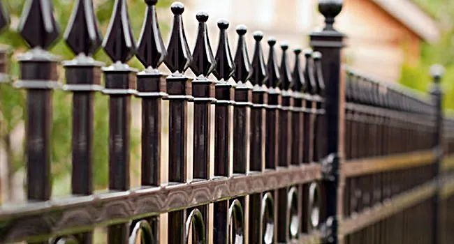 Black metal fence with pointed finials along a blurred residential walkway