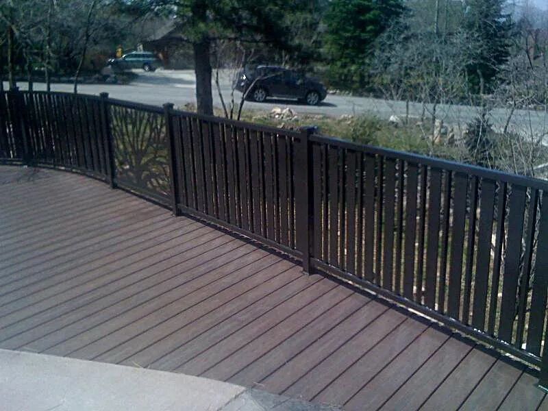 Wooden deck with black railing overlooking a street and parked cars beyond.