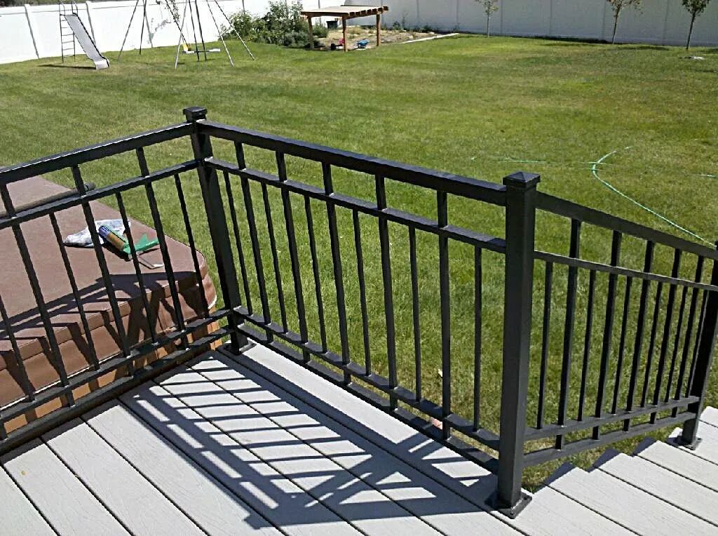 Black metal deck railing by a wooden deck beside a grassy yard and ramp.