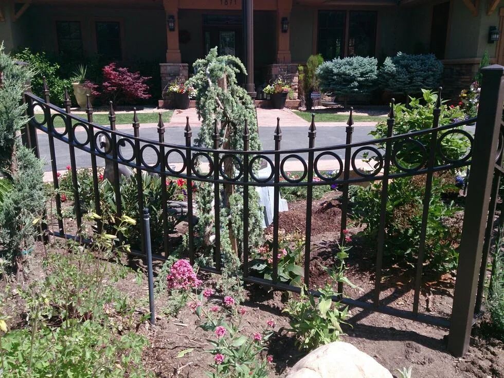 Black wrought-iron fence around a flower-filled courtyard with a house in the background