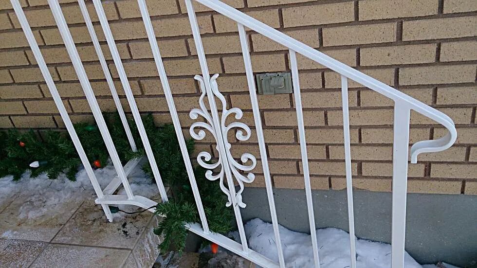 White metal porch railing with decorative scrollwork beside a brick house and stone steps
