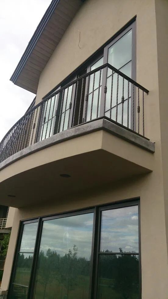 Two-story beige house with black balcony railings and large glass windows under an overcast sky