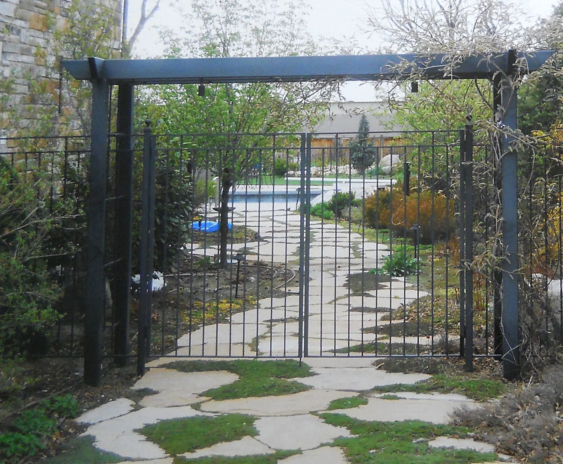 Garden path behind a black metal gate with stone stepping stones and trees