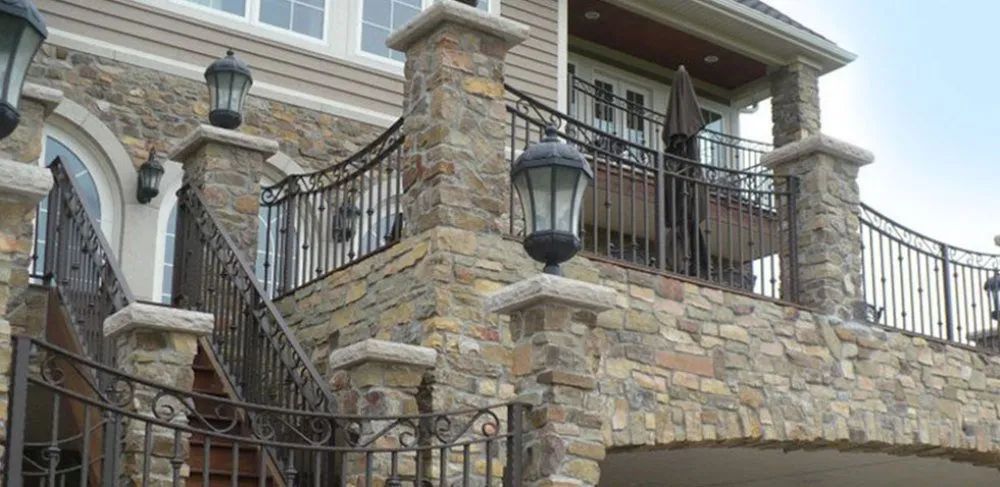 Stone house exterior with curved staircase, black wrought-iron railings, and upper balcony