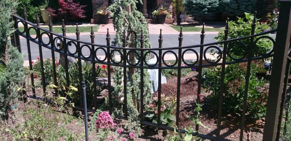 Black wrought-iron garden fence with circular details in a flower-lined park path