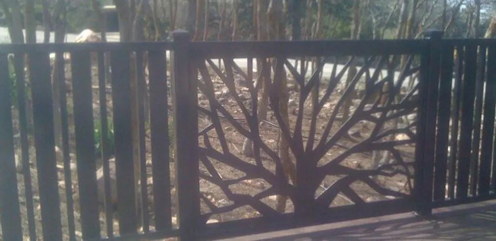 Black metal fence with a decorative tree silhouette panel in a sunlit outdoor setting