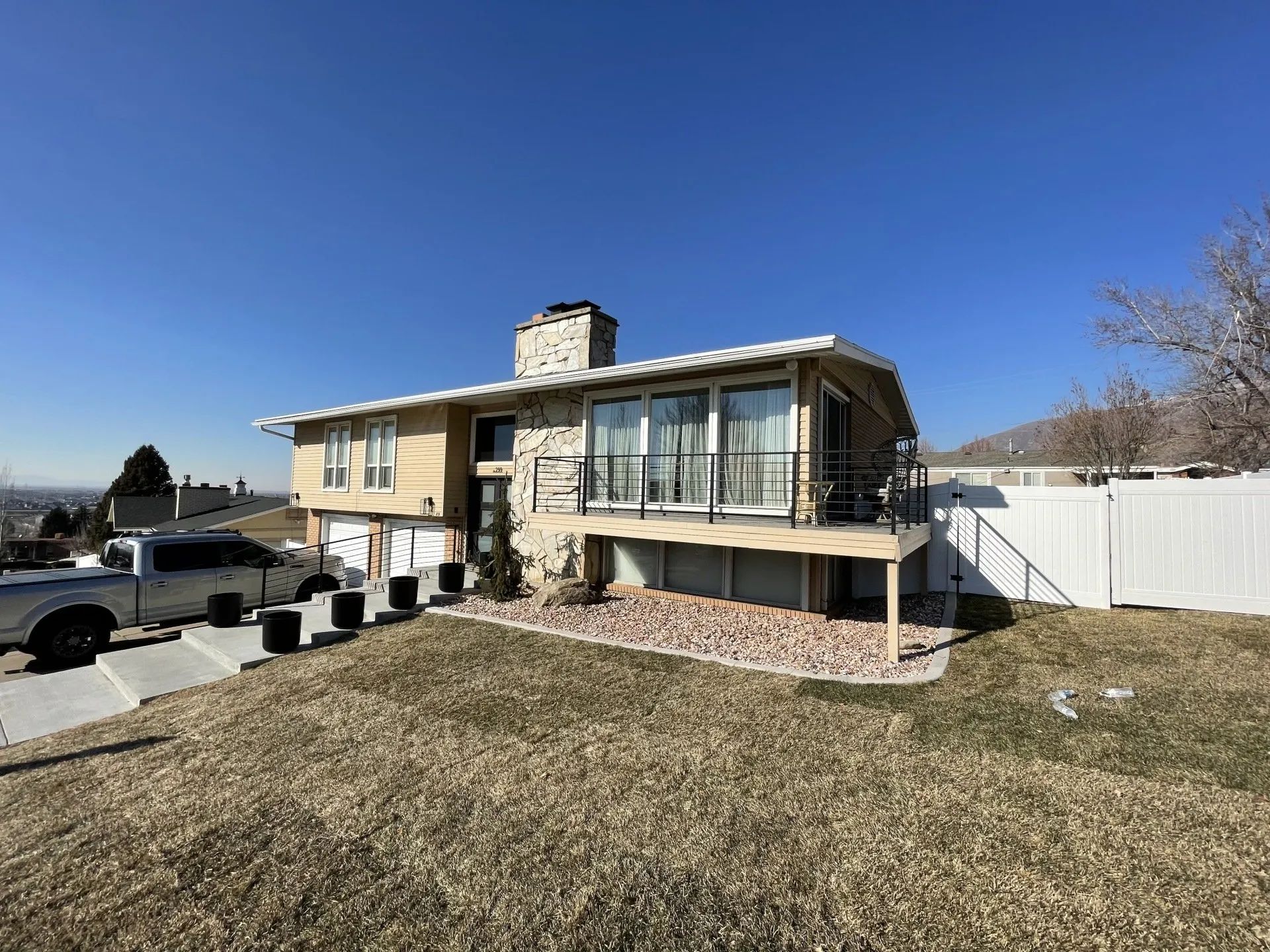 Suburban house with a stone chimney, front porch, and large yard under a clear blue sky
