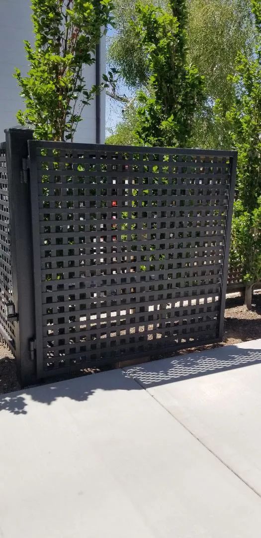 Black perforated metal privacy screen beside a sidewalk with a small tree behind it