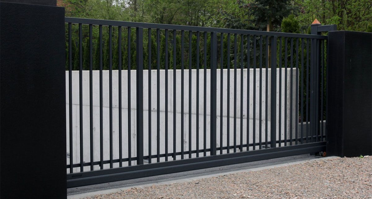 Black metal sliding gate in front of a light gray wall on a gravel driveway
