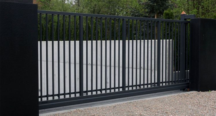 Black metal sliding gate in front of a light gray wall on a gravel driveway