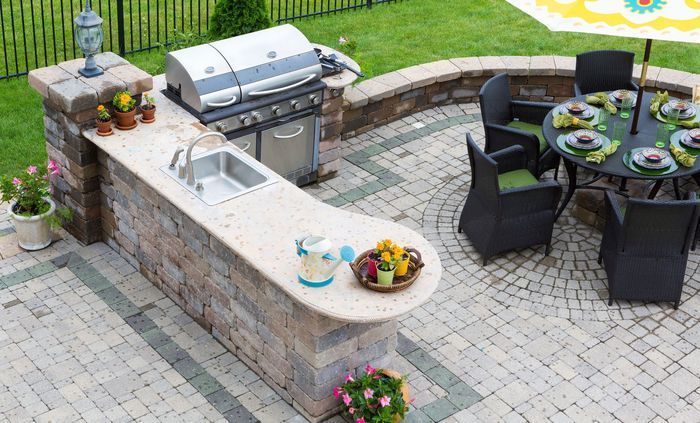 Outdoor kitchen with grill, sink, and seating area on a brick patio.