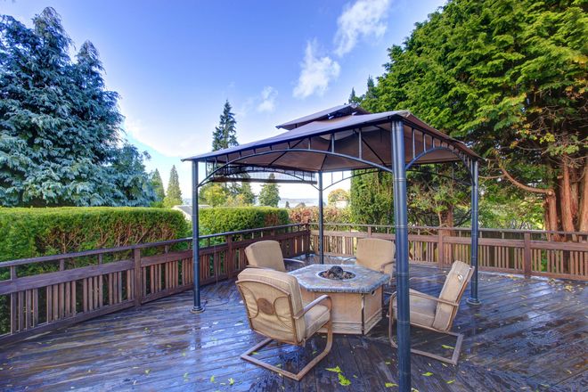 Patio with gazebo, seating, and fire pit on a wooden deck surrounded by trees.