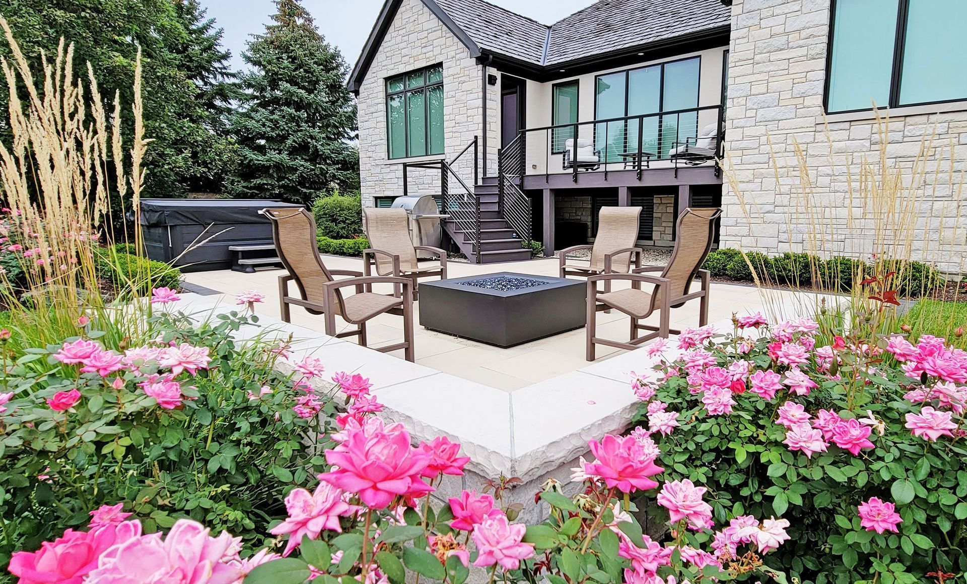 Stone house with a patio, fire pit, and chairs surrounded by pink roses.