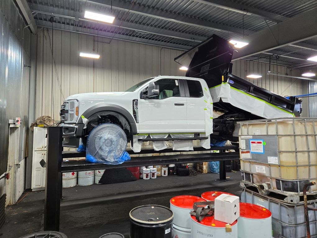 White garbage truck on a lift, rear view. Inside a repair bay.