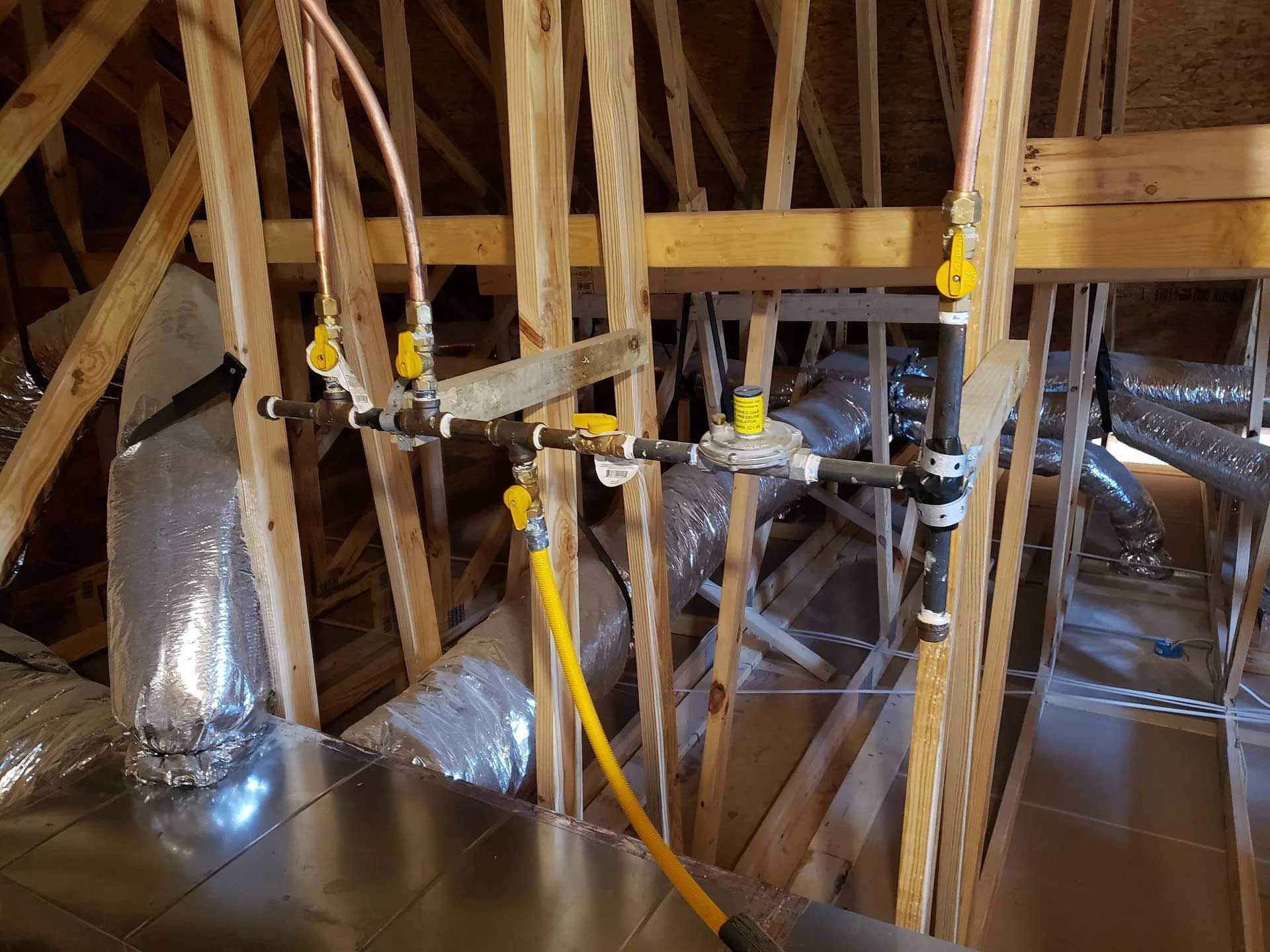 Gas lines with valves and flexible yellow tubing in an attic, running between wooden beams.