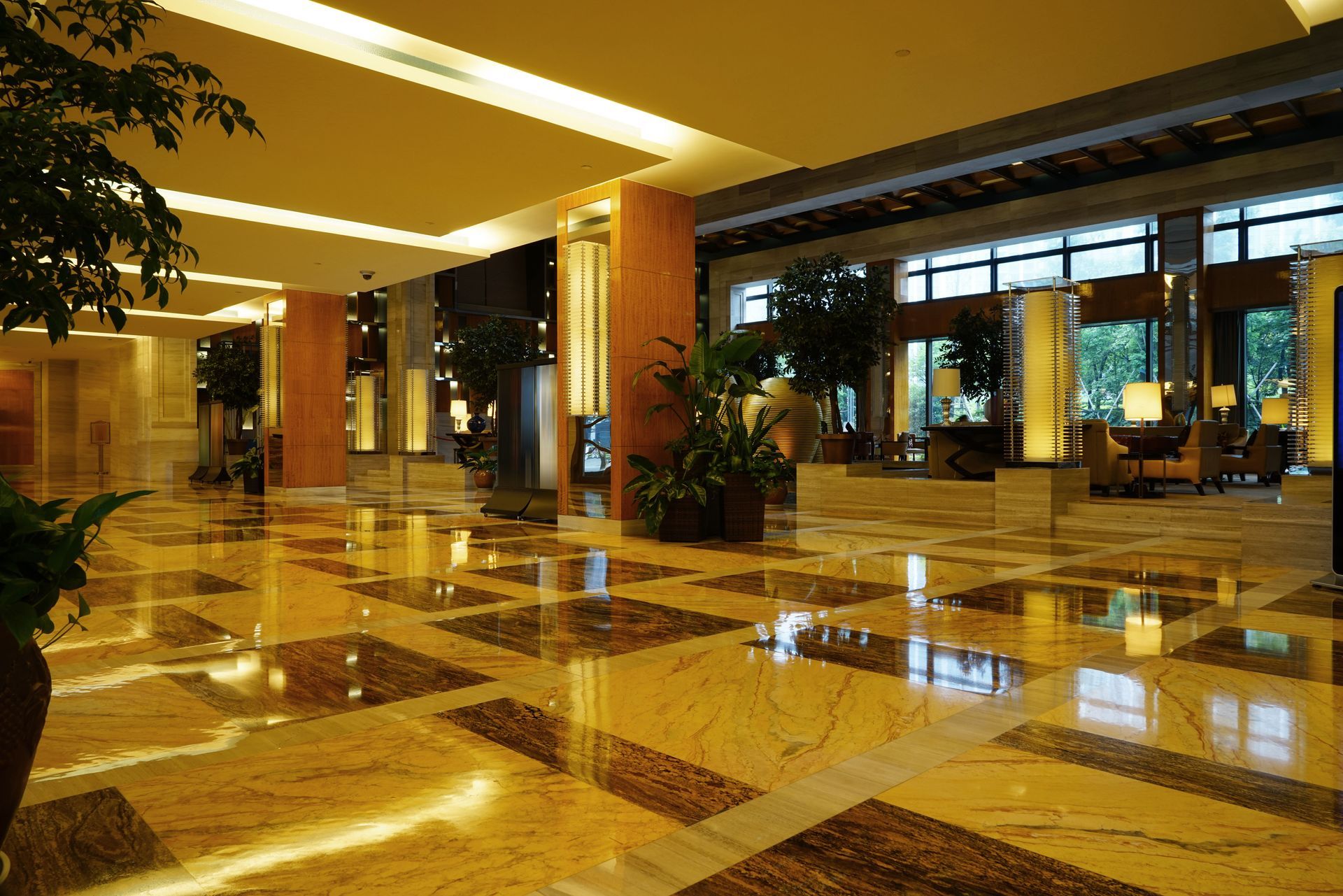 Hotel lobby with reflective, patterned marble floor and tall columns. Natural light and greenery.