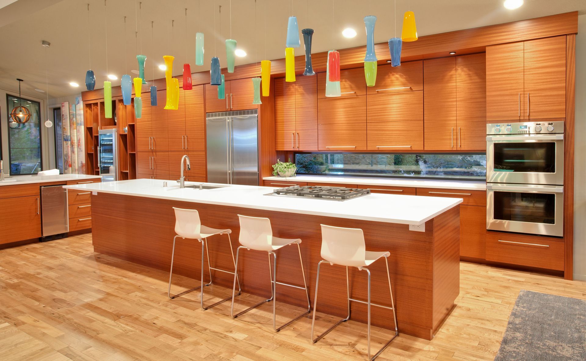 Modern kitchen with wood cabinets, island, and colorful hanging lights.