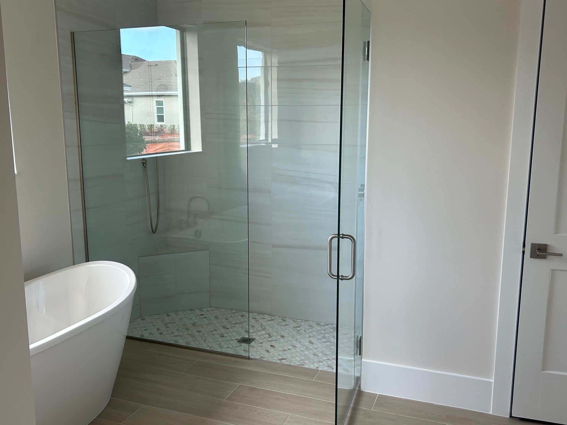 Modern bathroom with a glass-enclosed shower, white bathtub, and light-colored tile floor.