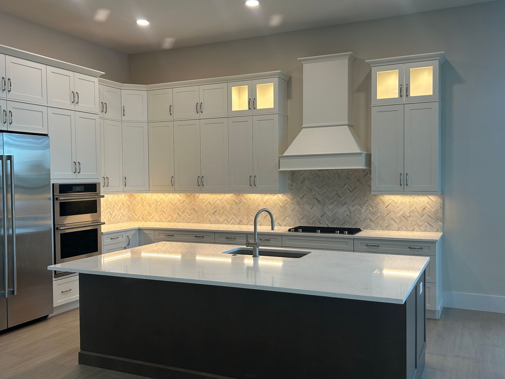 White kitchen with dark gray island, stainless steel appliances, and decorative backsplash.