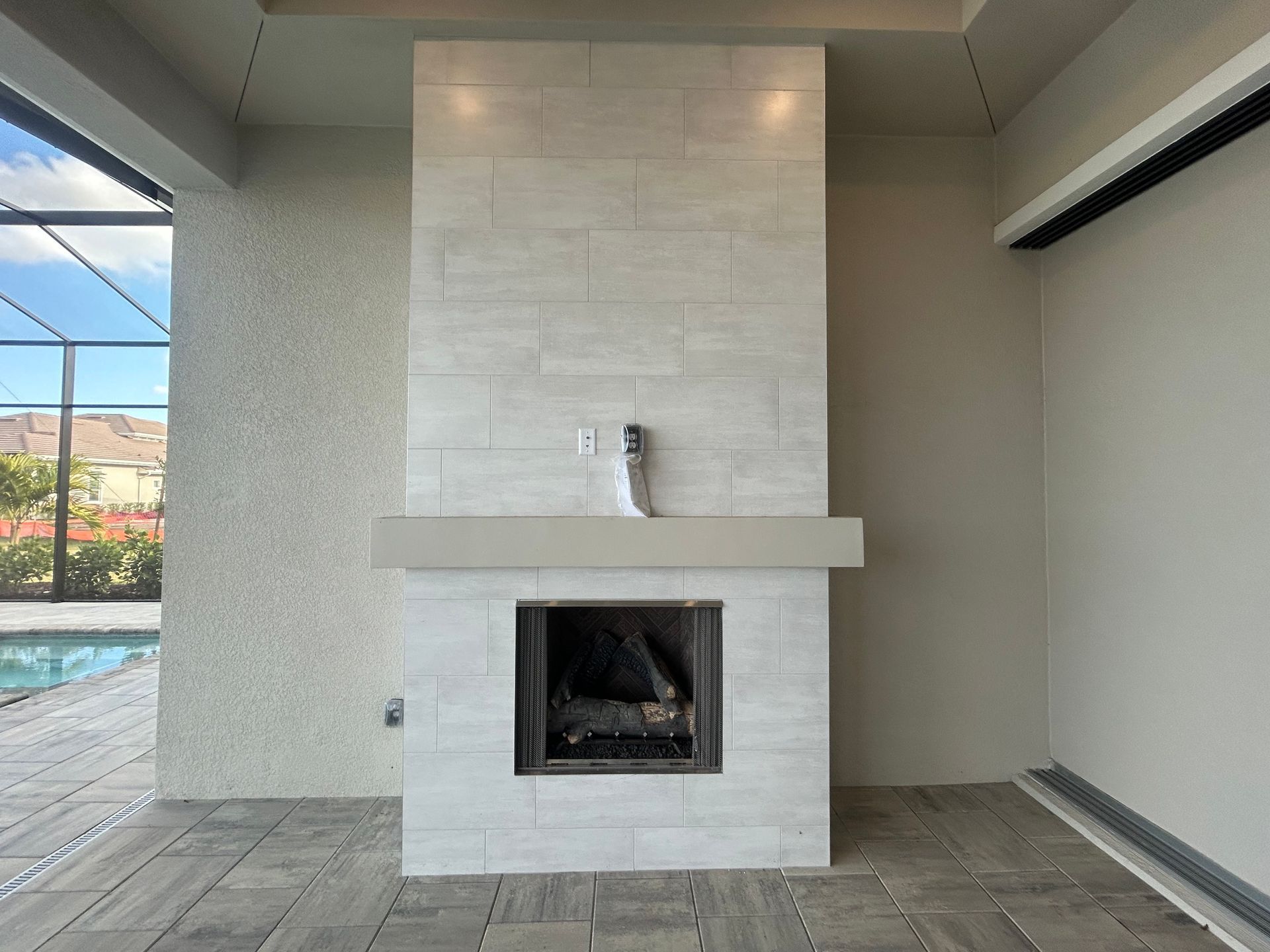 Fireplace with light stone tiles, a stone mantle, and a dark interior. Located outside near a pool.