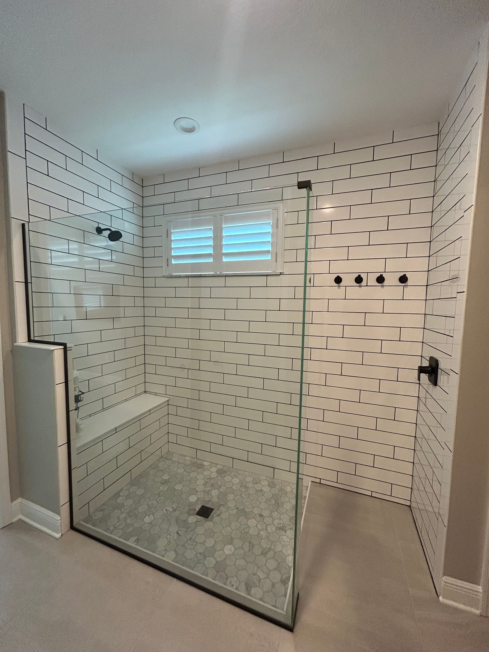 Modern shower with patterned white tile, glass enclosure, and a built-in bench.