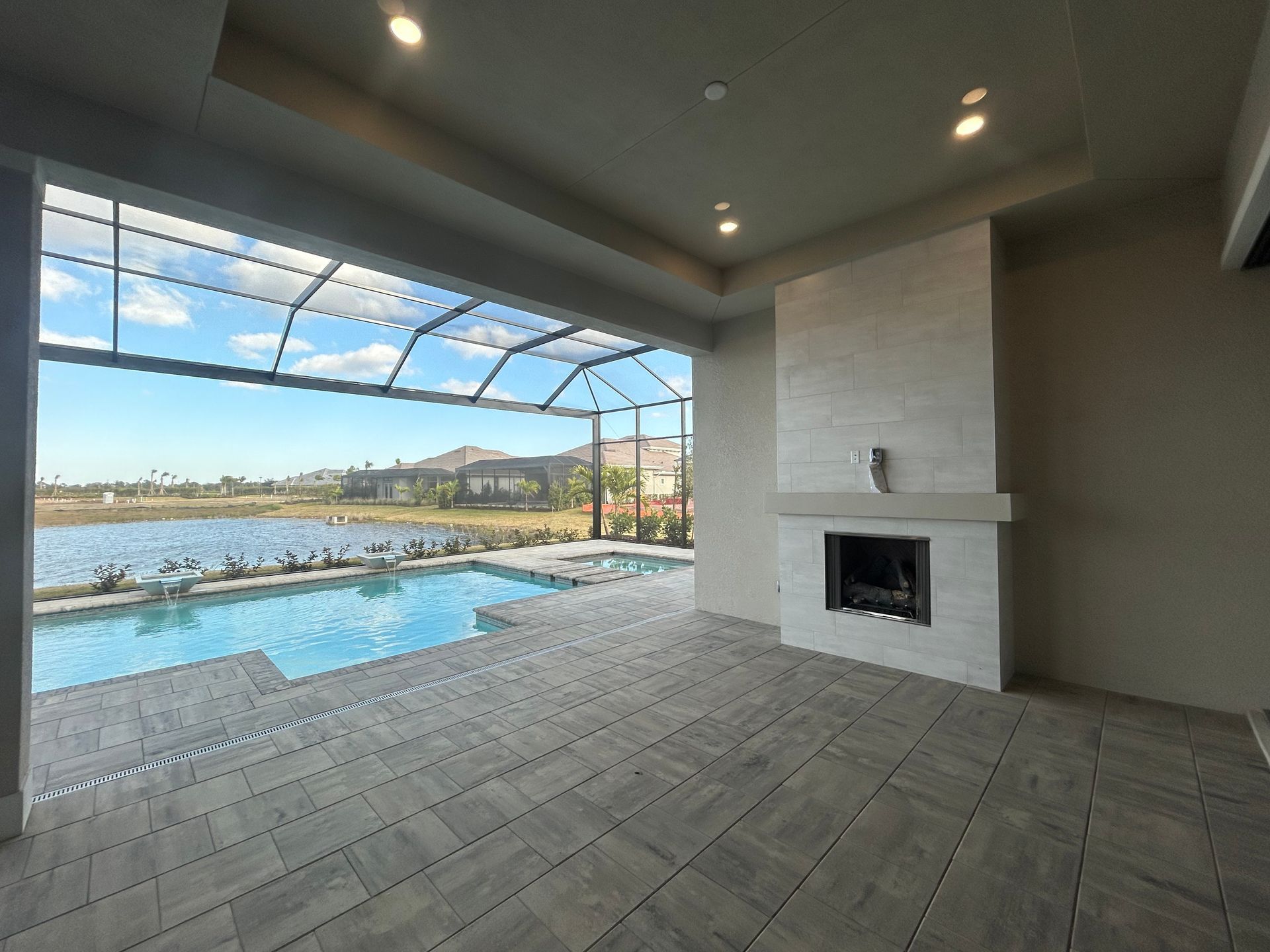 Covered outdoor patio with pool, lake view, fireplace, and gray tiled floor.