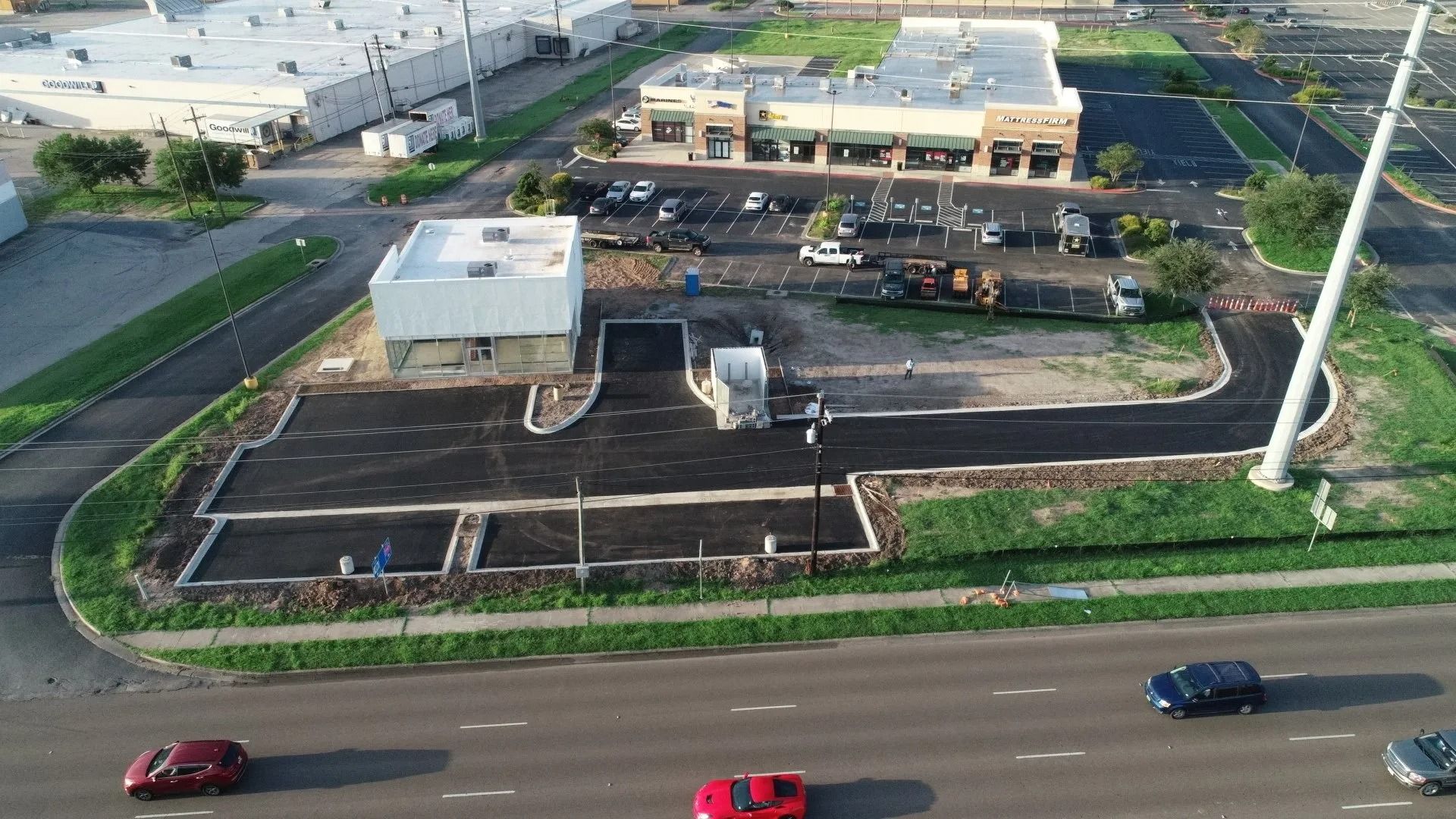 Aerial view of a roadside commercial lot with parked vehicles, a small building, and a main road in front.