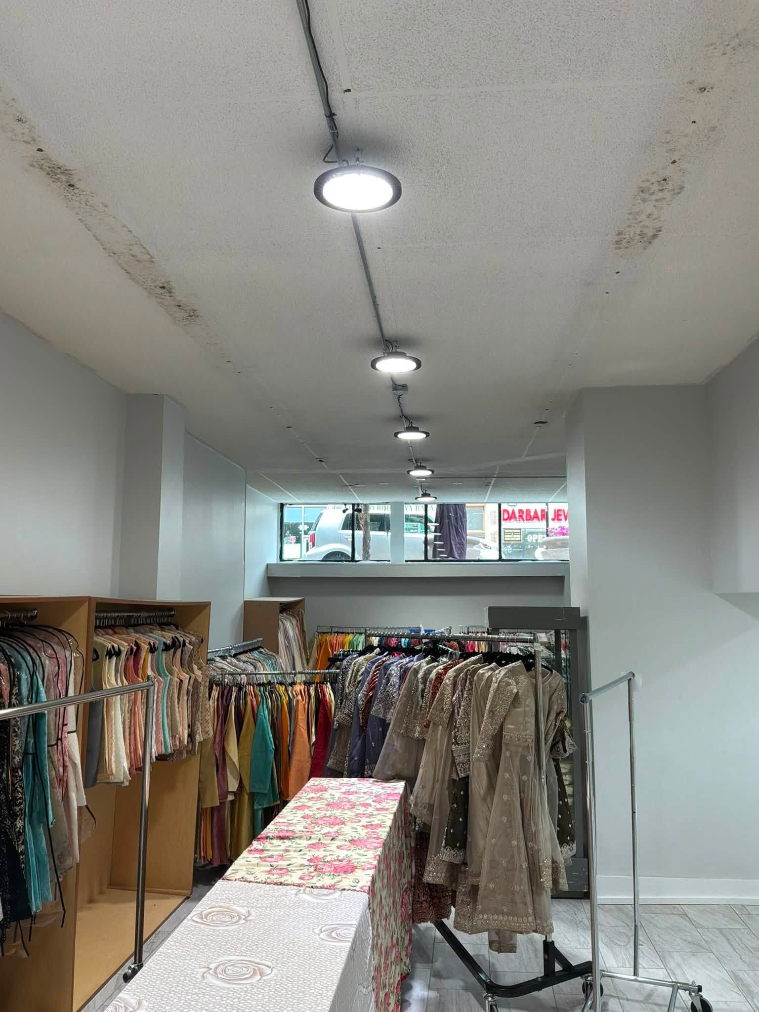 Clothing store aisle with racks of dresses and a floral display table under ceiling lights.