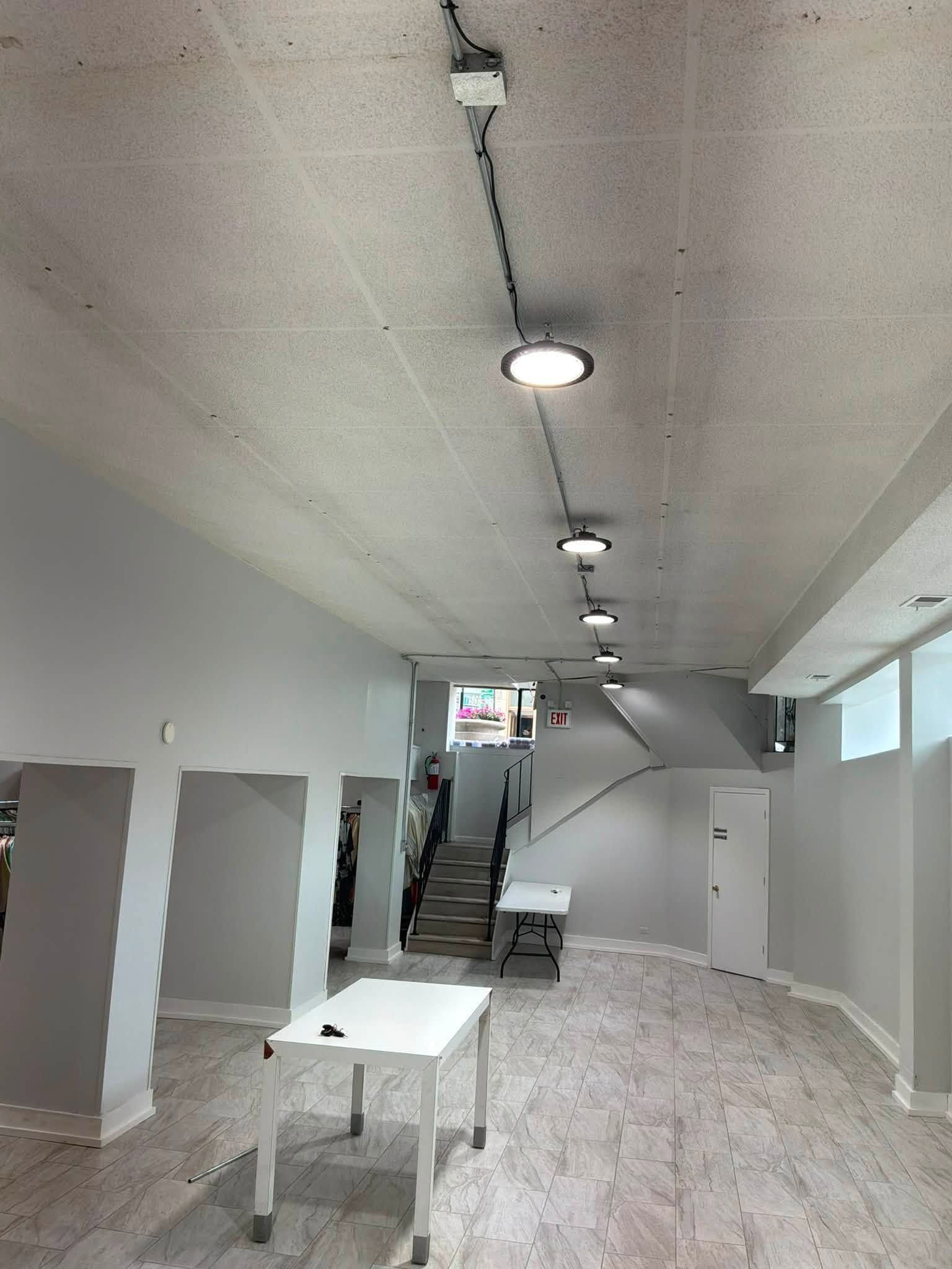 Empty white hallway with exposed ceiling lights, a table, and stairs leading upward