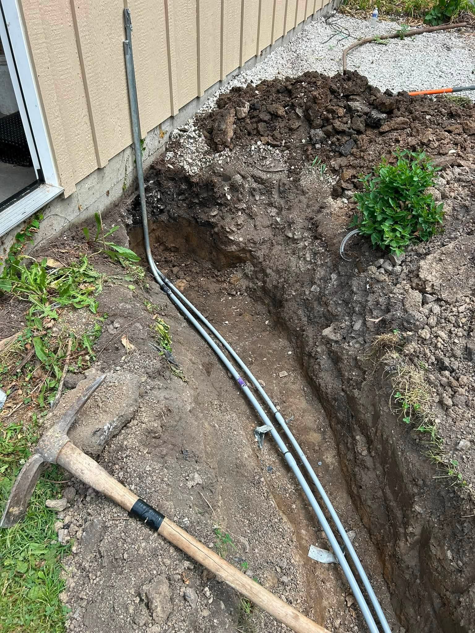 Trench beside a house with exposed cables and a shovel in dirt.
