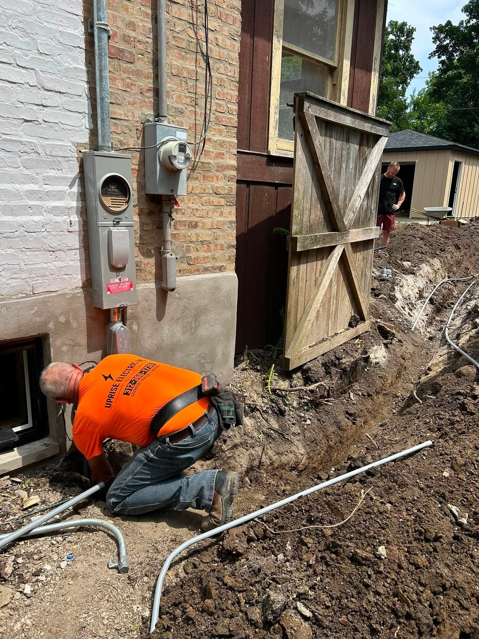 Worker in orange vest kneels by a basement wall, repairing or digging near a foundation opening.