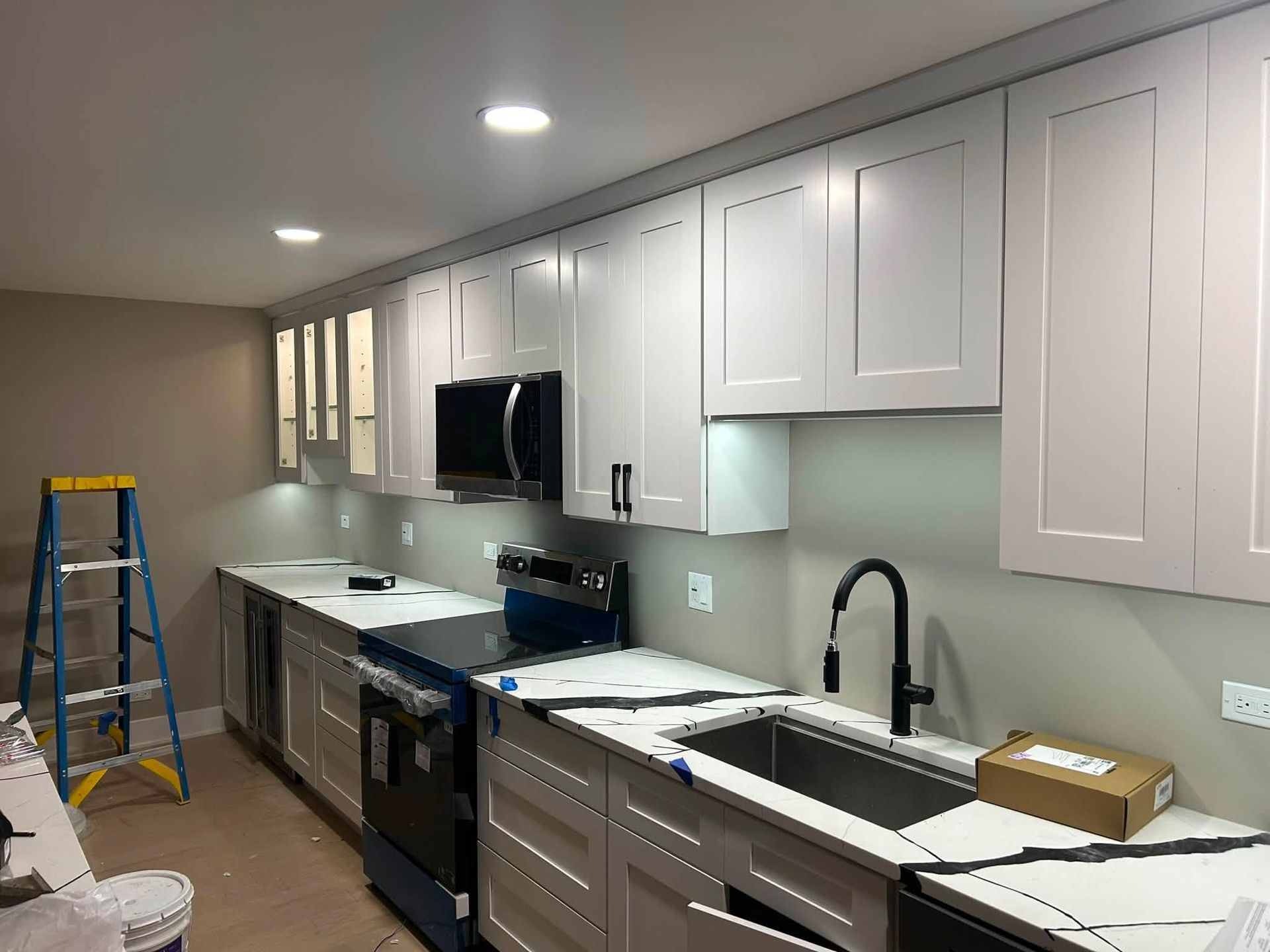 Kitchen remodel with white cabinets, black countertops, and appliances under bright recessed lighting