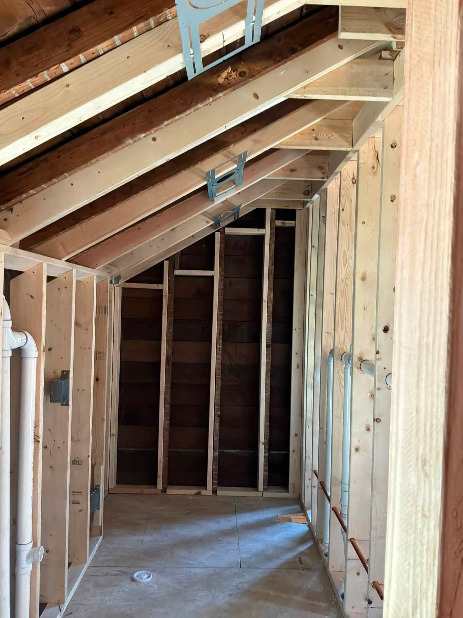 Unfinished attic hallway with exposed wooden framing and slanted ceiling beneath roof trusses.